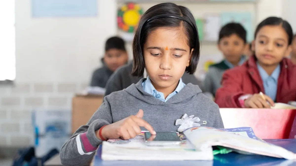 कक्षा में किताब के साथ स्मार्टफ़ोन से पढ़ती छात्रा (प्रतीकात्मक तस्वीर)
